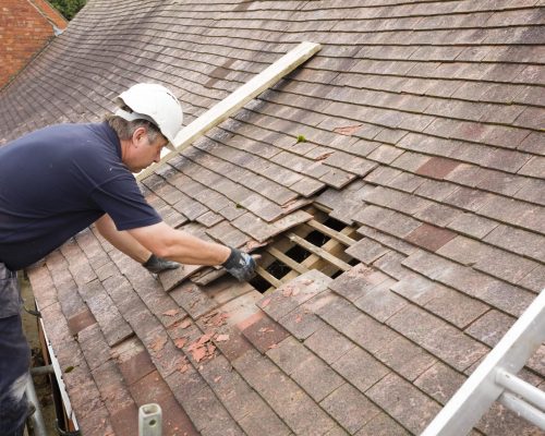Builder removing old clay tiles from a pitched roof UK Roof Replacement